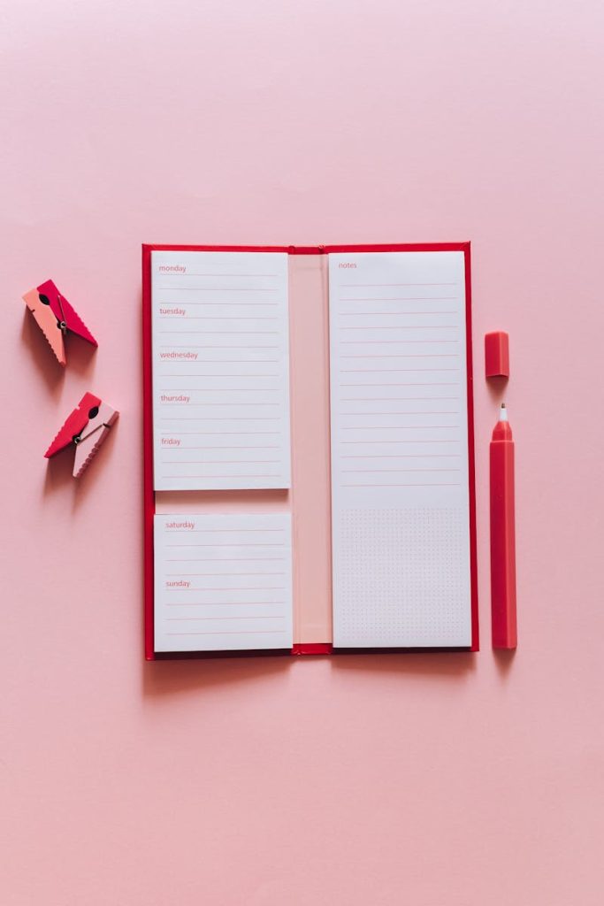 Open notepad with clips and a pen on a pink background, perfect for planners.